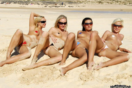 Caucasian chicks wander a beach while wearing nipple pasties and thongs