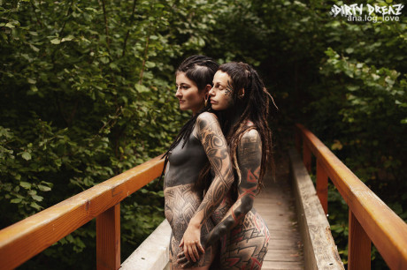 Heavily tattooed lesbians hold each other while totally nude on a bridge