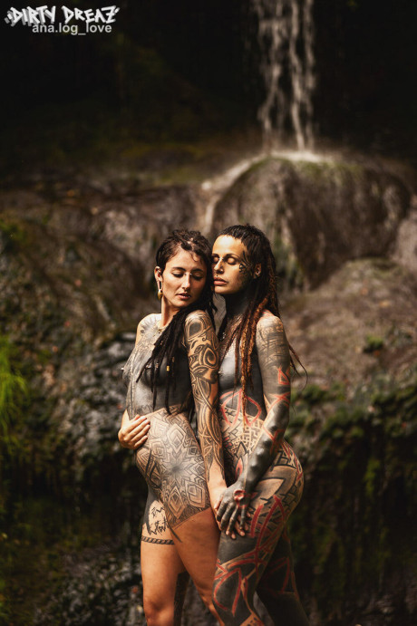 Heavily tattooed lesbians hold each other while totally nude on a bridge