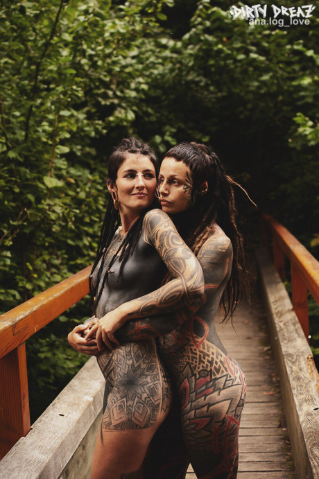 Heavily tattooed lesbians hold each other while totally nude on a bridge
