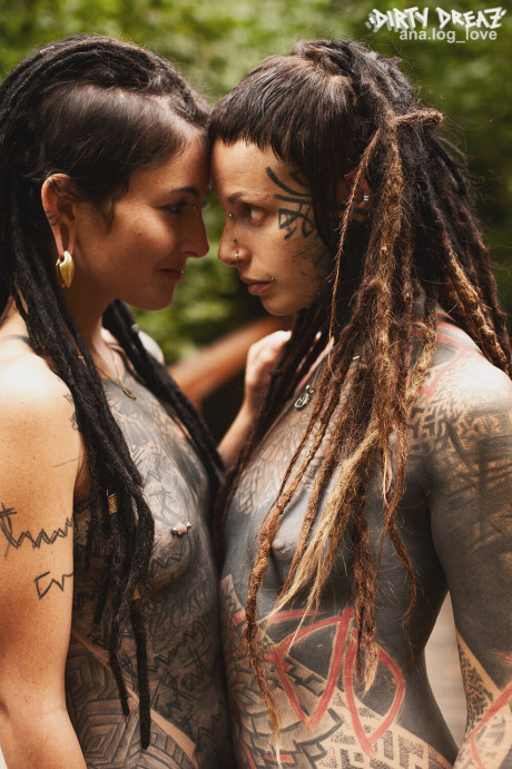 Heavily tattooed lesbians hold each other while totally nude on a bridge