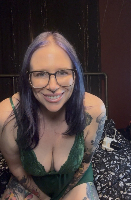 Tattooed female with purple hair exposes her vagina and large tits on a bed