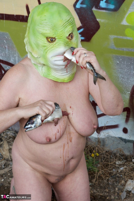 Undressed British lady chick Speedy Bee eats a fish while wearing a costume mask