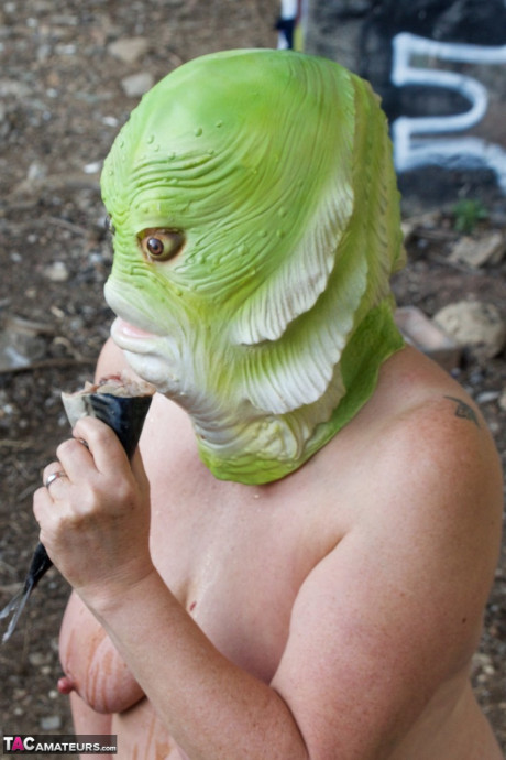 Undressed British lady chick Speedy Bee eats a fish while wearing a costume mask