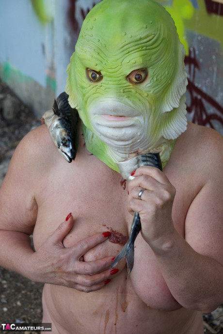 Undressed British lady chick Speedy Bee eats a fish while wearing a costume mask