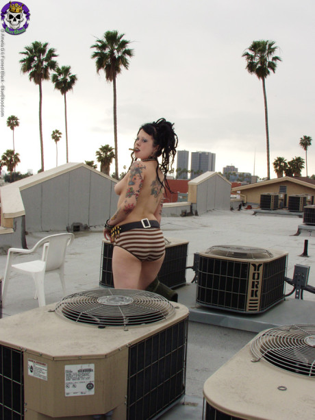 Tattooed punk Eva Klench smokes a cigar on a rooftop in platform boots
