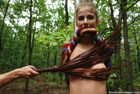 Thin blondy slut girl lady is flogged while tied to a tree in the forest