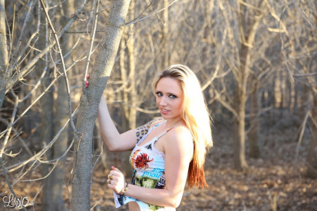 Blondie amateur Lily Xo places her forearm over her boobs while in a forest