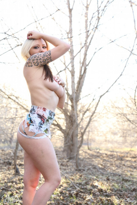 Blondie amateur Lily Xo places her forearm over her boobs while in a forest