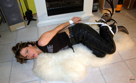 Clothed Caucasian female Jenna struggles on a rug while hogtied