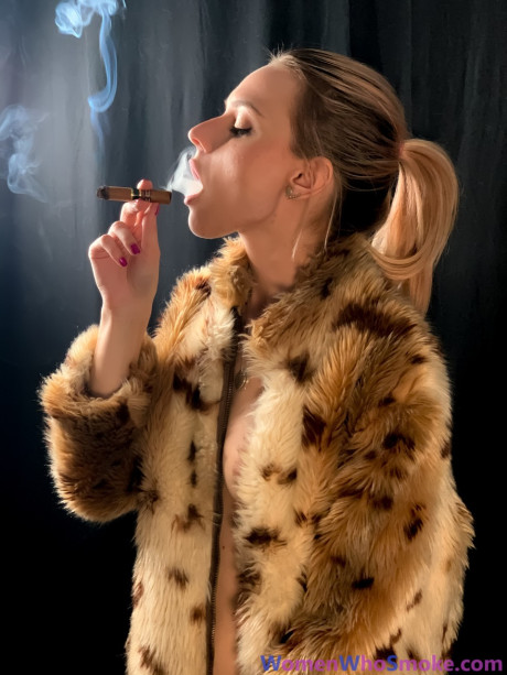 Blondy with a ponytail poses in her fur coat as she smokes a cigarette