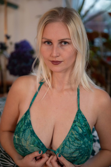 Busty yellow-haired strips naked and masturbates with a sex toy on a bed