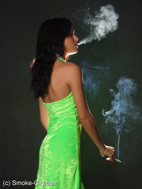 Dark haired young wears a lime dress and pointy heels while smoking