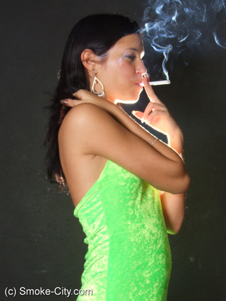 Dark haired young wears a lime dress and pointy heels while smoking