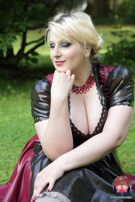Overweight yellow-haired Darkwing Zero models on a lawn in a rubber dress