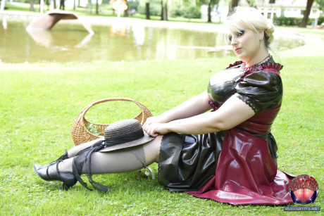 Overweight yellow-haired Darkwing Zero models on a lawn in a rubber dress