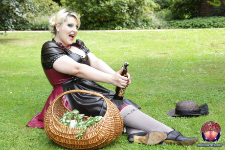 Overweight yellow-haired Darkwing Zero models on a lawn in a rubber dress