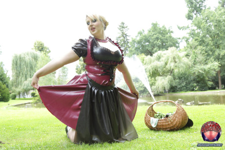 Overweight yellow-haired Darkwing Zero models on a lawn in a rubber dress