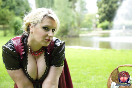 Overweight yellow-haired Darkwing Zero models on a lawn in a rubber dress