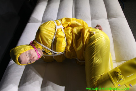Caucasian girl woman Pia is ball gagged and hogtied in a yellow rain suit