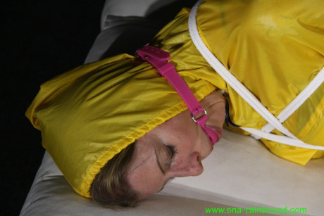 Caucasian girl woman Pia is ball gagged and hogtied in a yellow rain suit