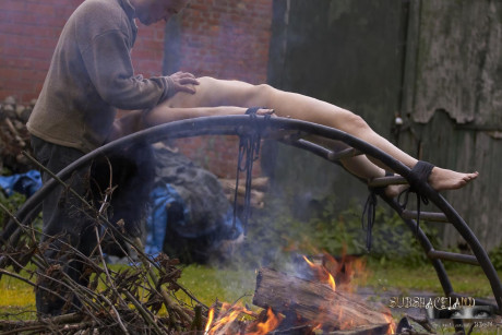 Naked brunette Ally Style is roasted over a fire during BDSM training