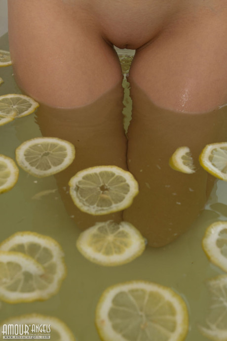 Cute blonde teenie sinks her bald twat into a tub filled with lemon slices