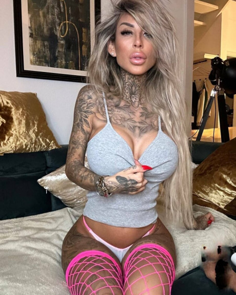 Tattooed amateur babe poses in pink fishnets & flaunts her hot legs & cleavage