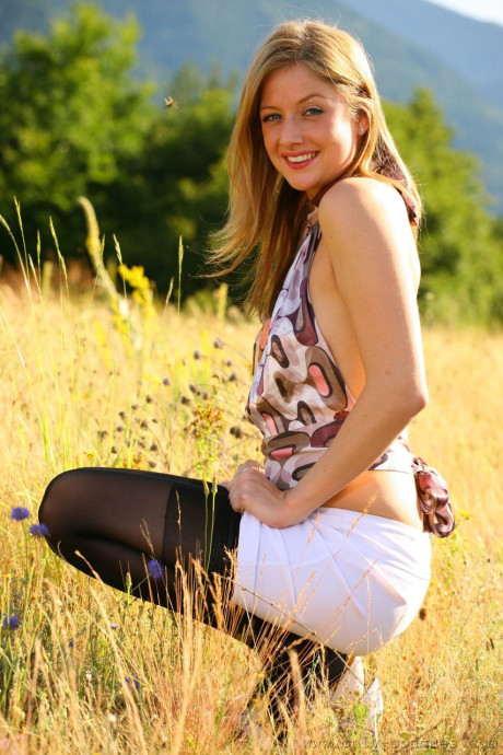 Pretty amateur teenie Nikki F squats as she poses in thong panties in the field