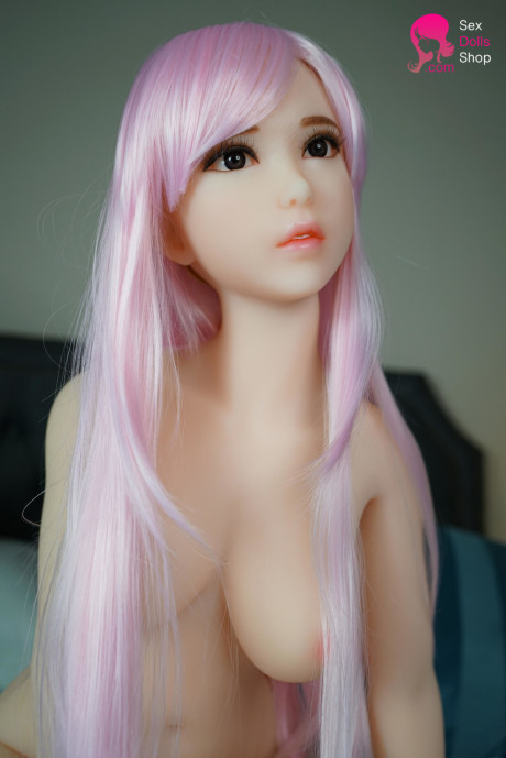 Pink-haired sex doll Phoebe flaunts her charming large breasts and nice ass on a bed