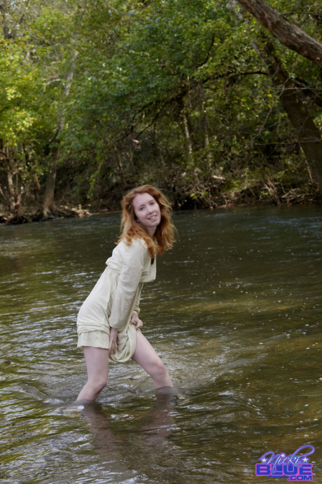 Natural ginger head Nicki Blue shows some leg while wading into a shallow stream
