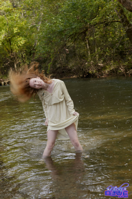 Natural ginger head Nicki Blue shows some leg while wading into a shallow stream