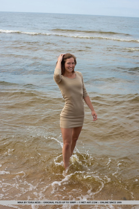 Tall teen Mina hangs wet clothes to dry while posing naked on a beach