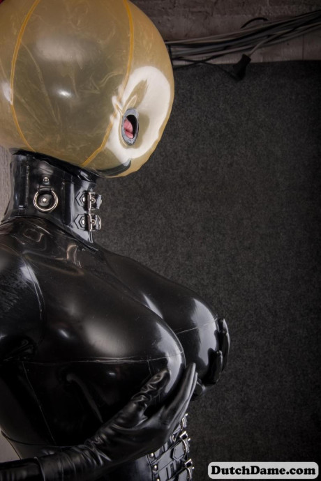 Latex attired slave is affixed with an inflatable hood in dungeon setting